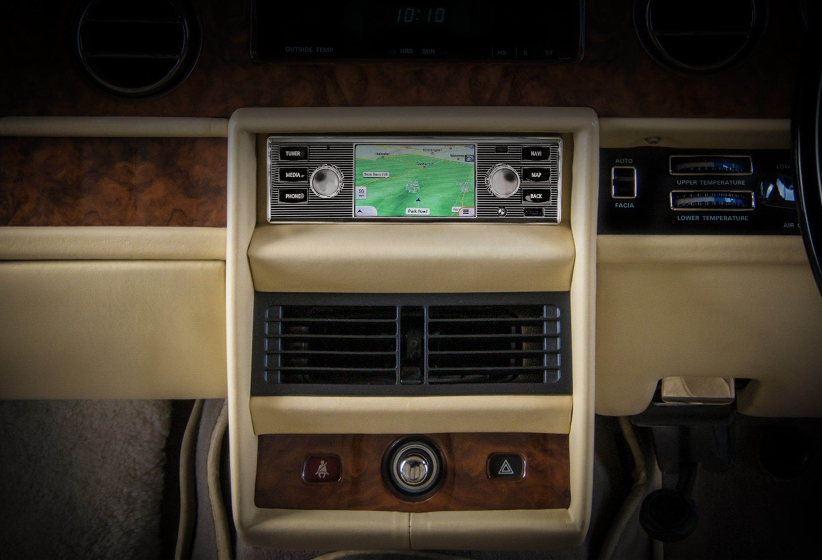 Centre console of a classic vehicle showing a navigation screen with map, air vents, and control buttons.