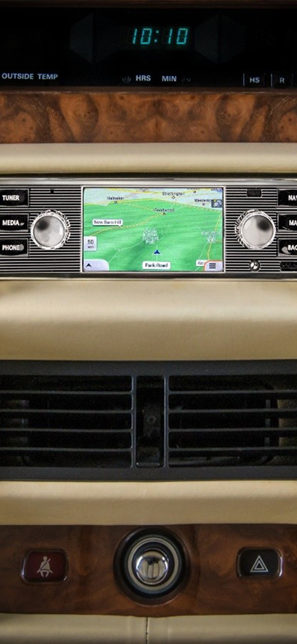 Centre console of a classic vehicle showing a navigation screen with map, air vents, and control buttons.