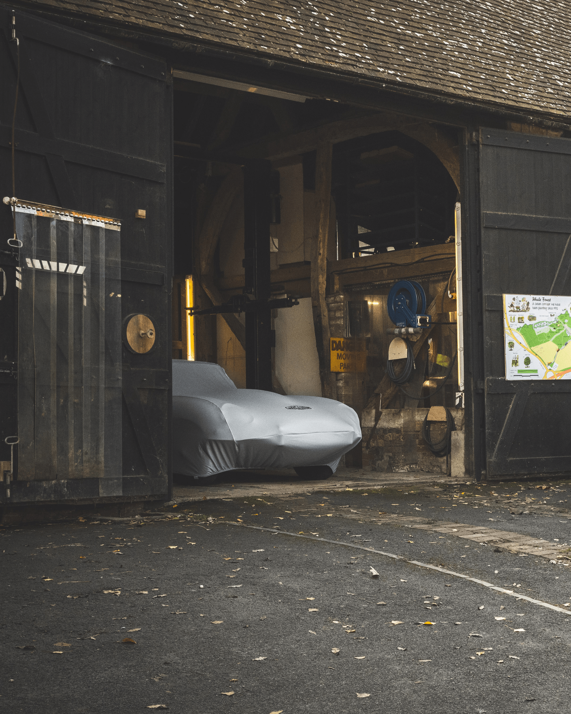 Covered Jaguar inside open black wooden barn with equipment and map on door.