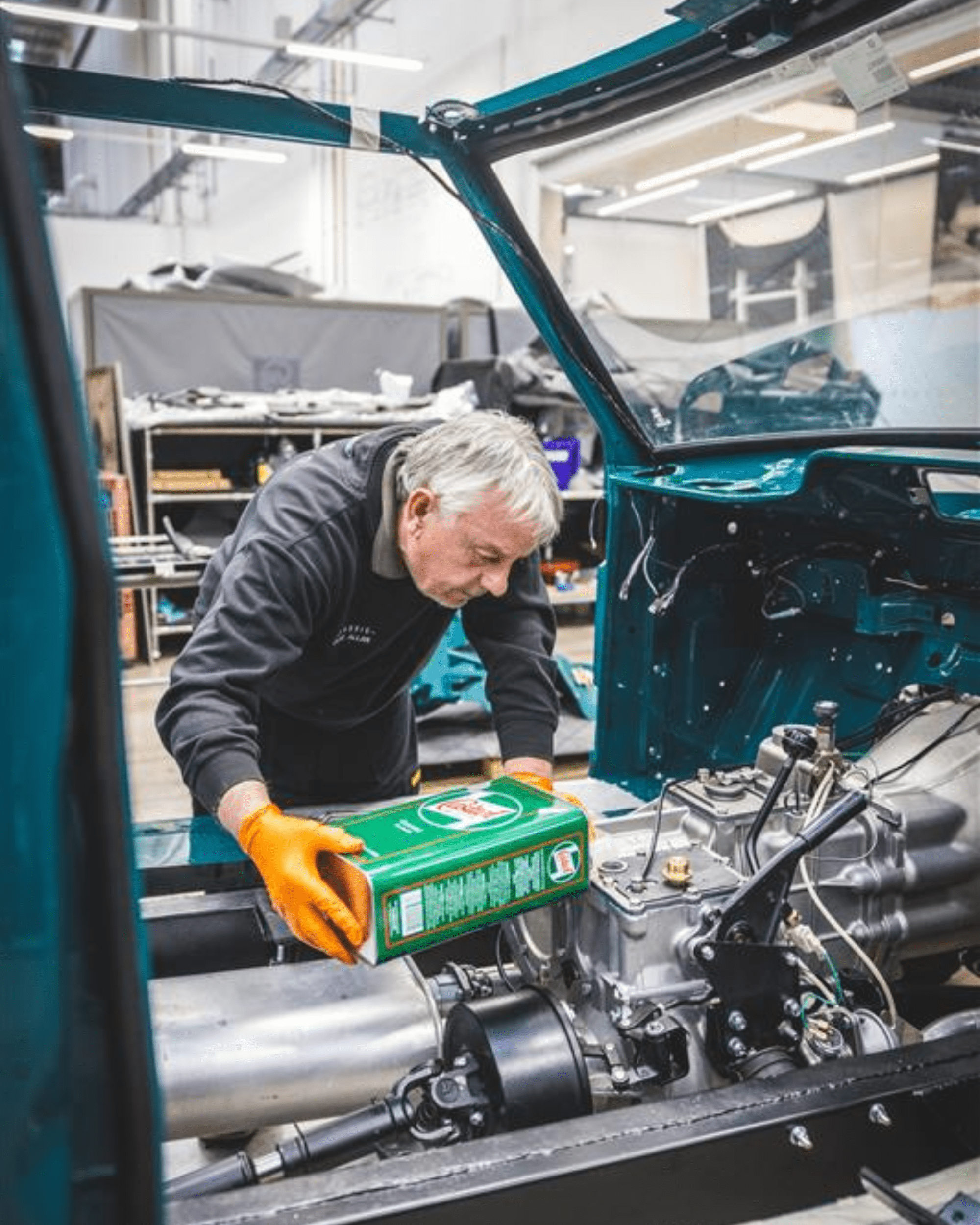 Person pouring Castrol oil fluid into car engine in workshop, wearing orange gloves.