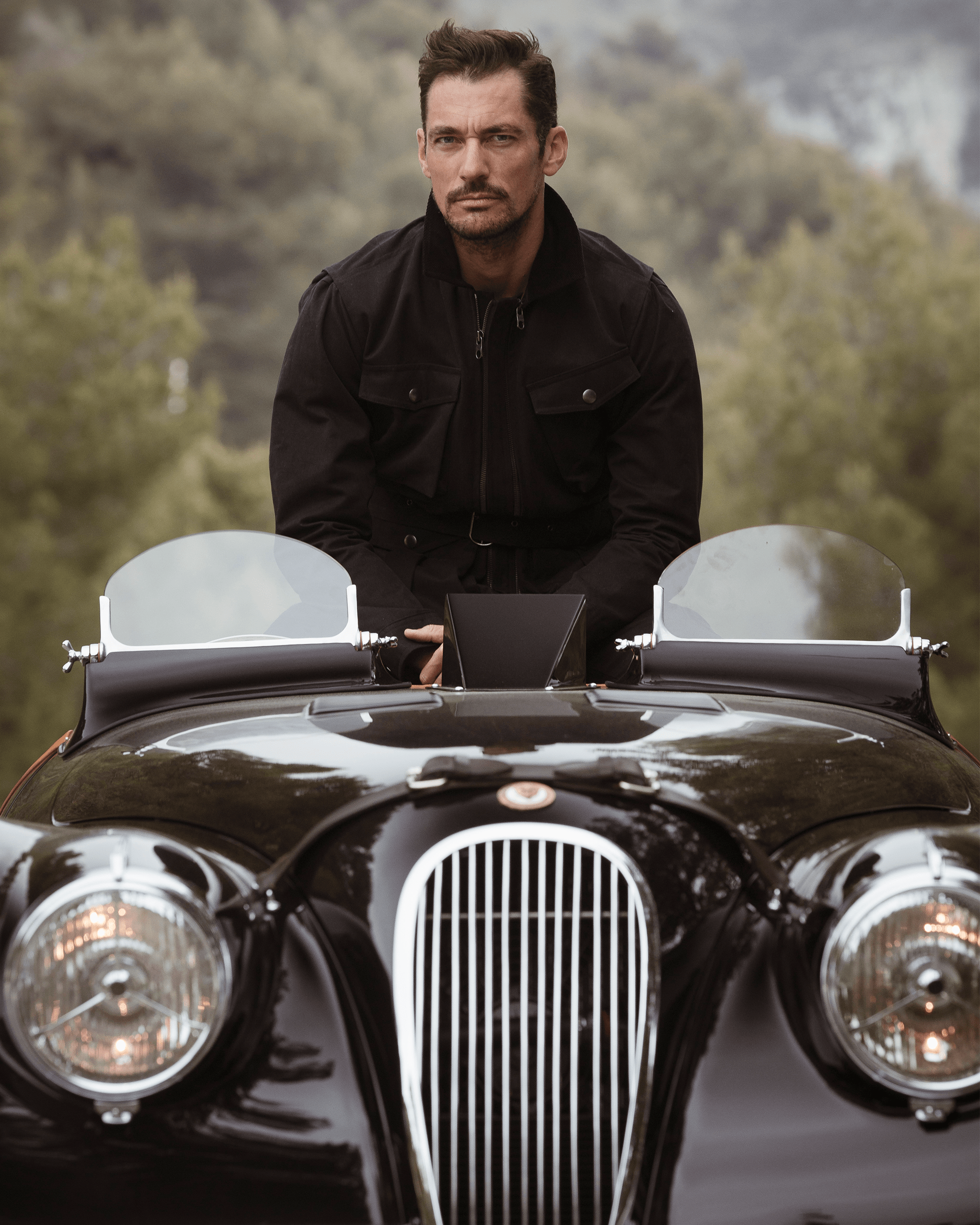 David Gandy in classic black Jaguar with twin windscreens and round headlights, outdoors.