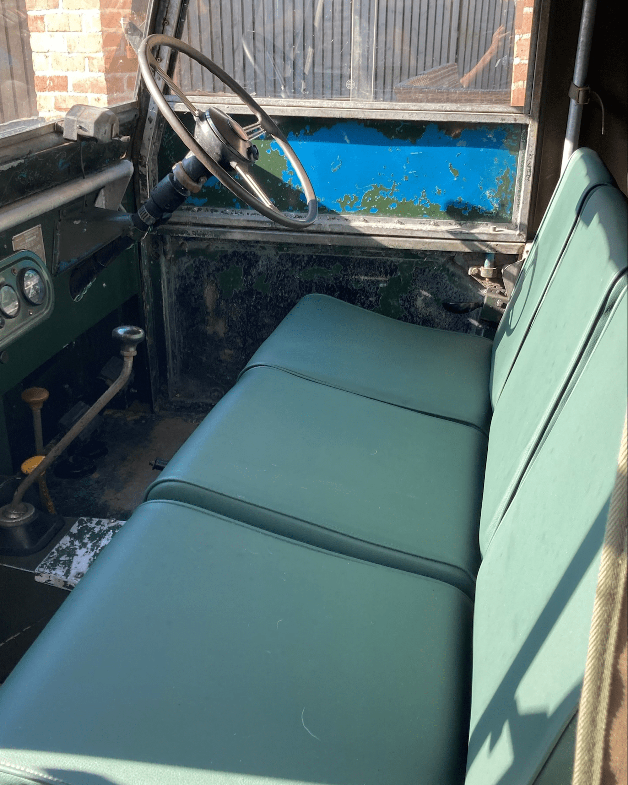 Interior of vintage Land Rover with green bench seat, worn dashboard, and manual controls.