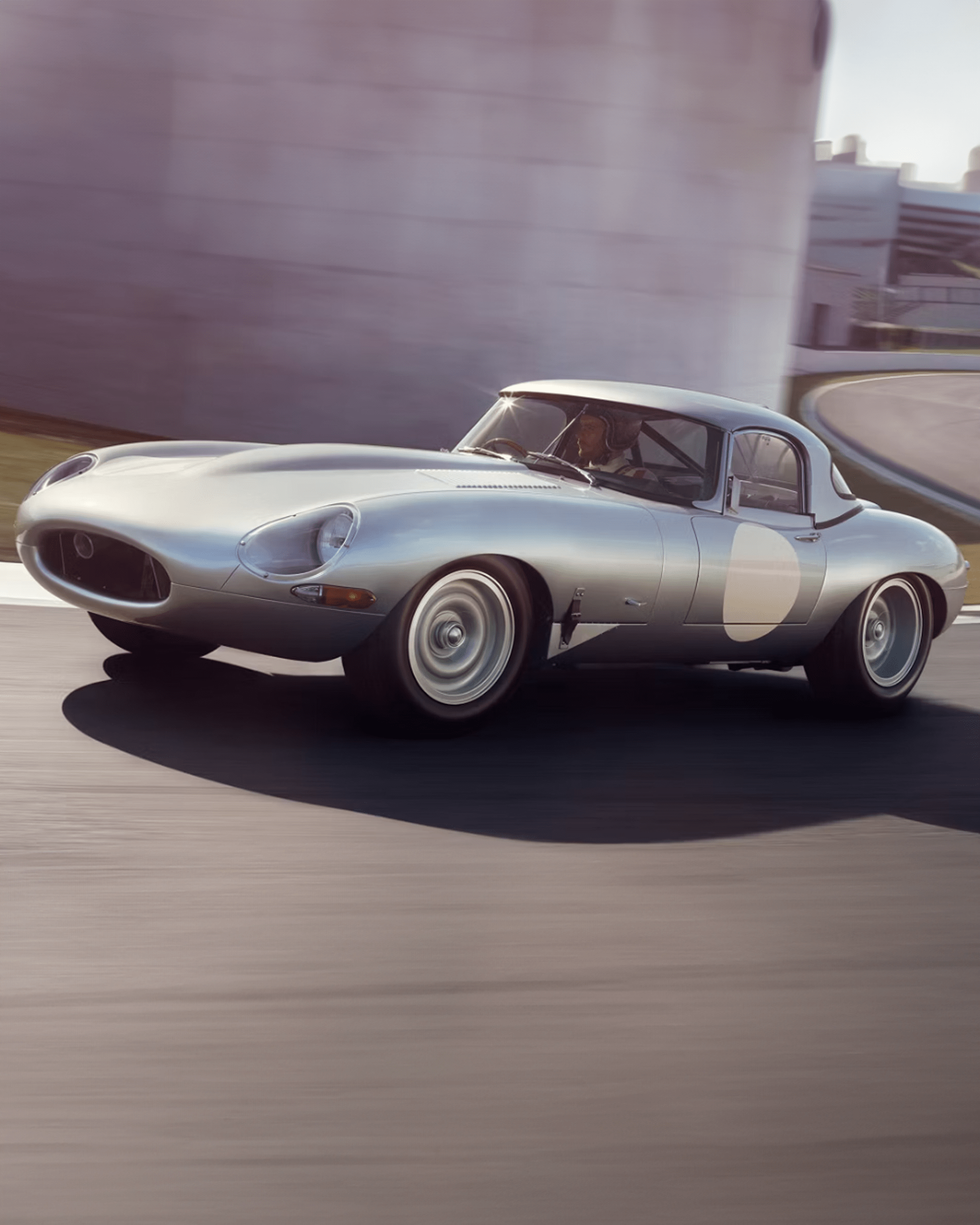 Silver Jaguar E-Type driving on a racetrack.