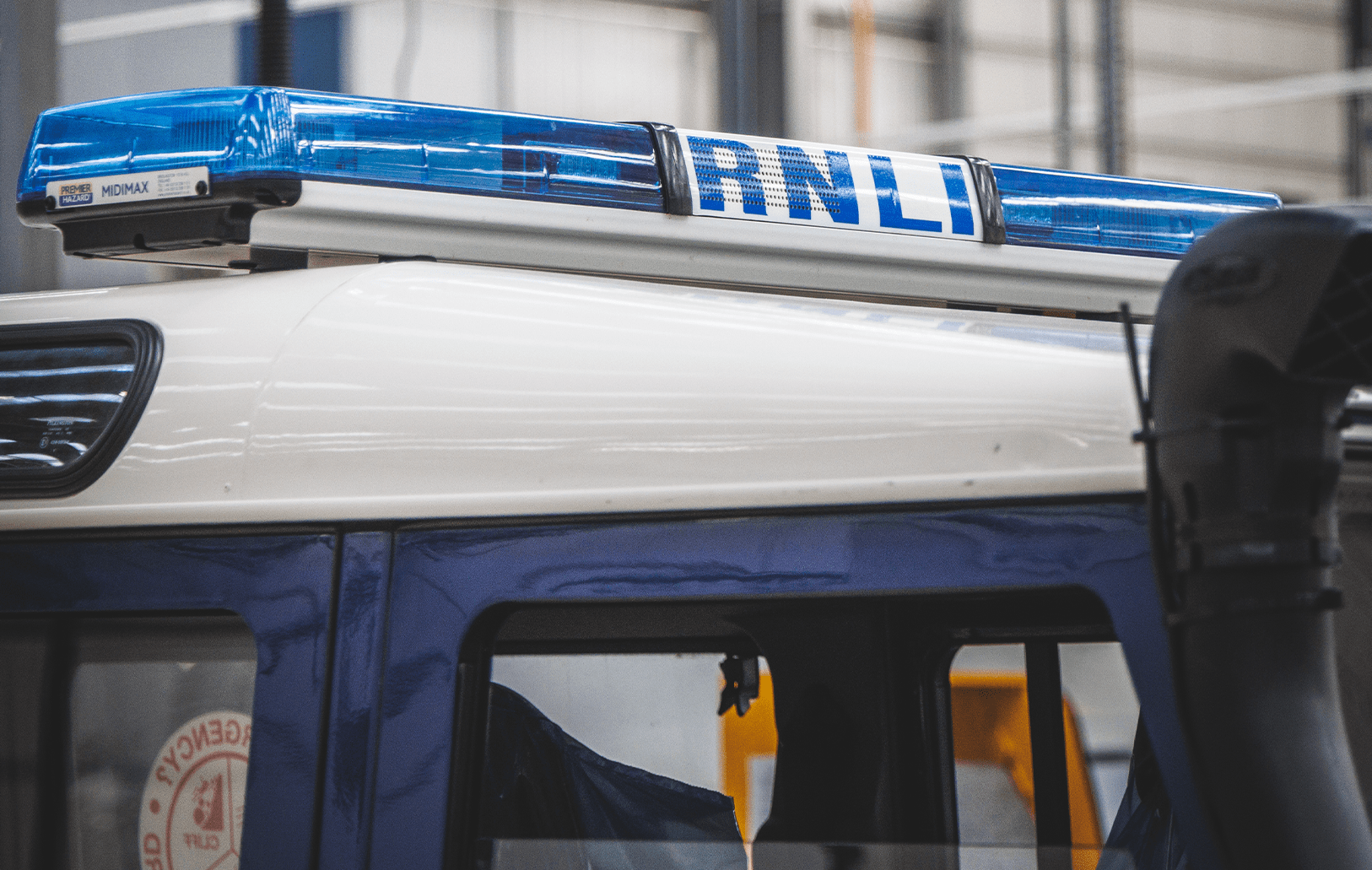 Vehicle roof with RNLI emergency light bar and 'EMERGENCY EXIT' sign visible through window.