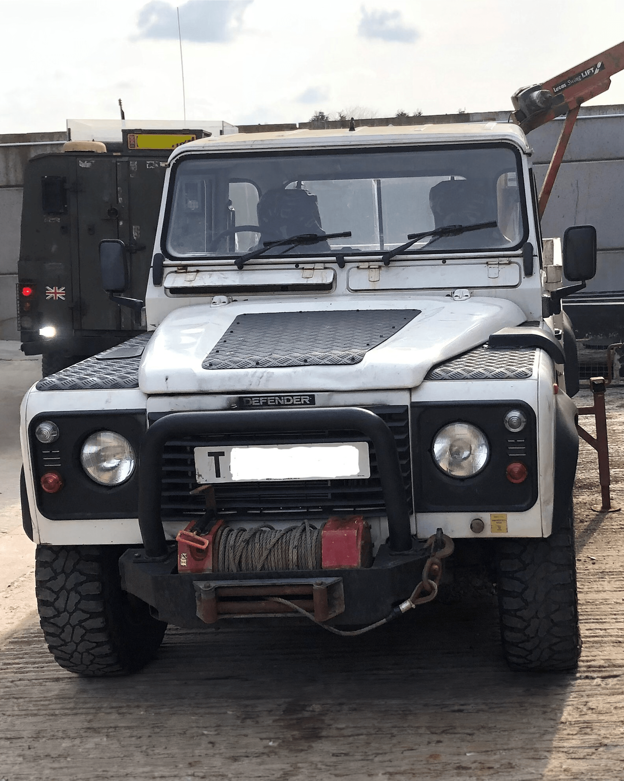 White Land Rover Defender with winch and off-road tires parked on concrete surface.