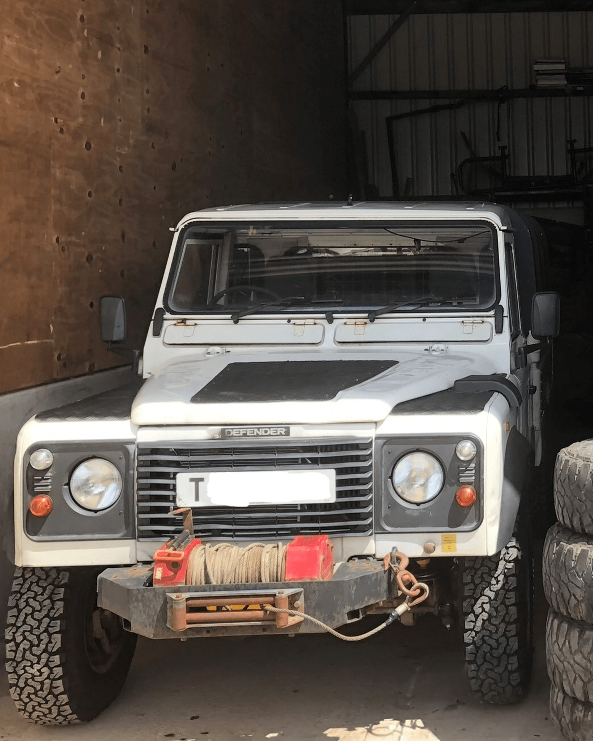 White Land Rover Defender with front winch parked in garage beside stacked tires.