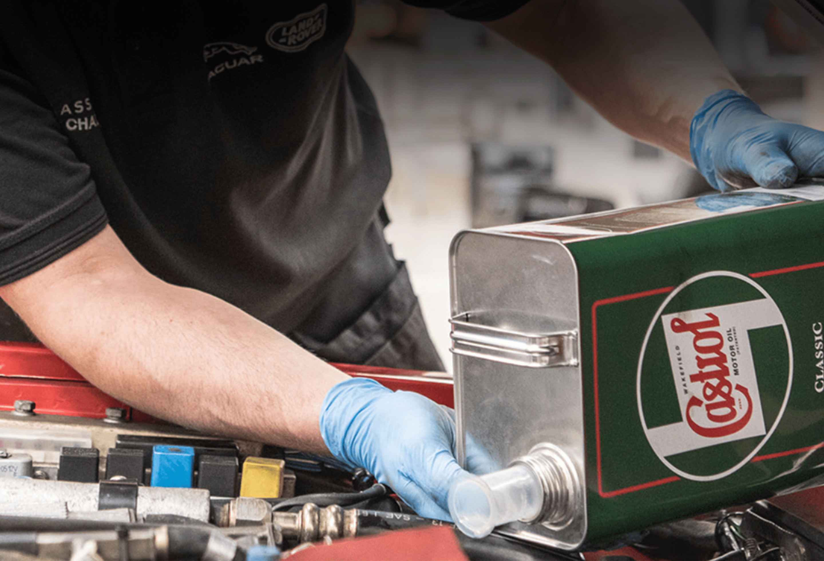 Person pouring Castrol Classic oil into engine, wearing Jaguar Land Rover Classic Works uniform shirt.