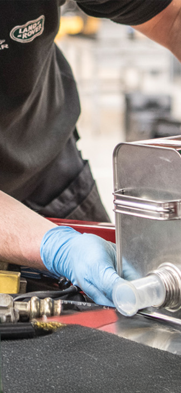 Person pouring Castrol Classic oil into engine, wearing Jaguar Land Rover Classic Works uniform shirt.