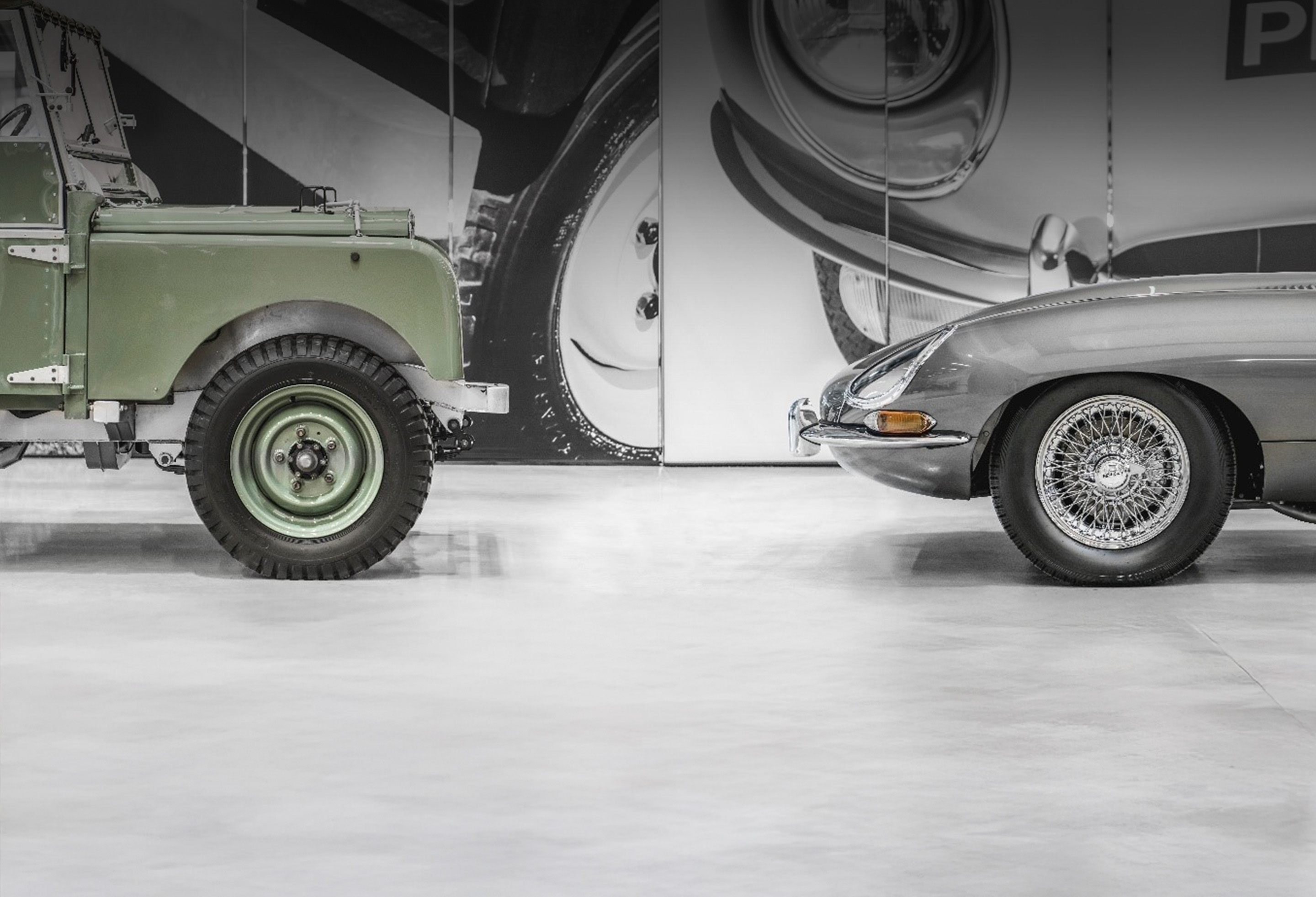 Front view of vintage green Land Rover and grey Jaguar E-Type facing each other in a showroom.