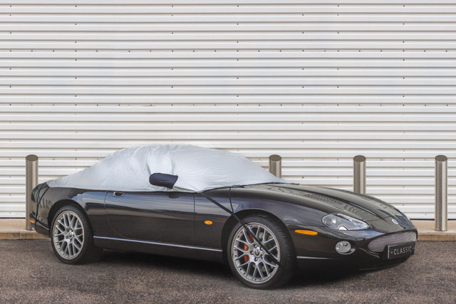 Half-Covered Jaguar parked in front of closed metal garage door.