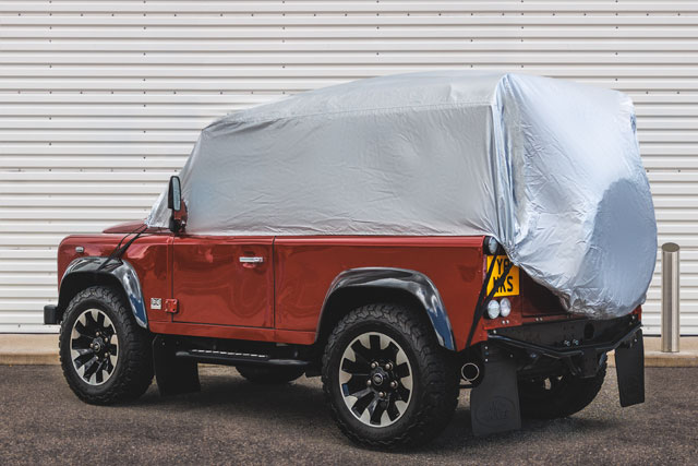 Half-Covered Land Rover parked in front of closed metal garage door.