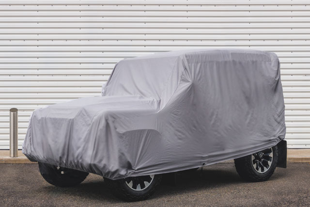Covered Land Rover parked in front of closed metal garage door.