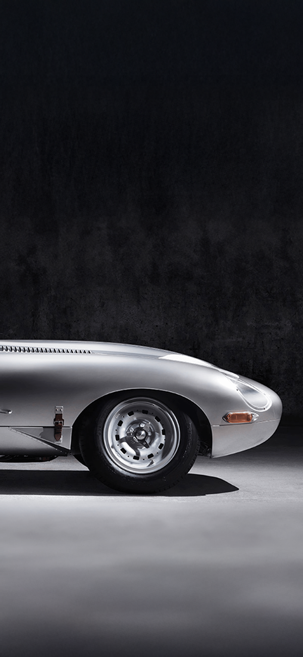 Classic silver E-Type with racing circle on door, side view.